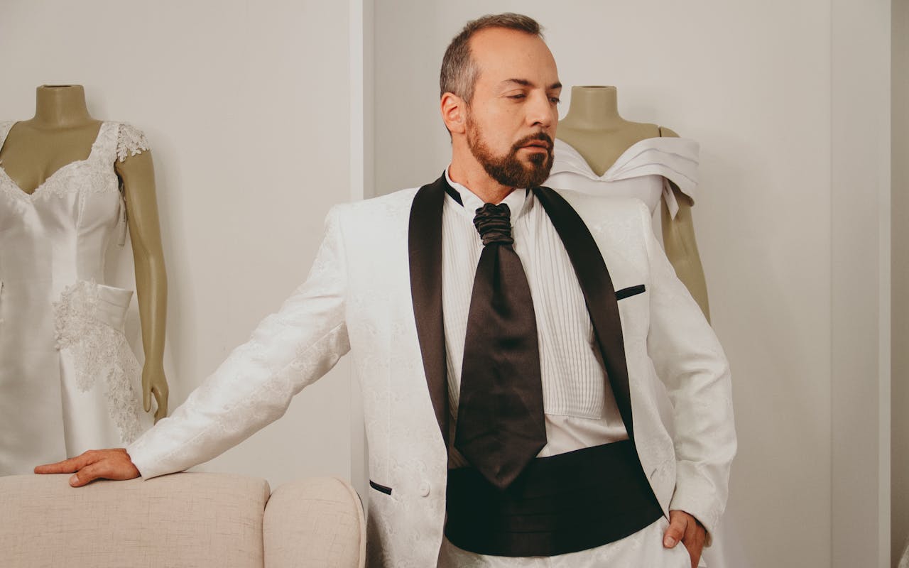Elegant groom in a stylish white suit poses in a wedding boutique setting.